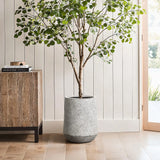 Potted tree with green leaves in a lightweight, durable MgO planter featuring a gray and white speckled texture, beside a wooden cabinet against a light paneled wall.