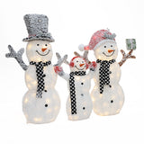 Three illuminated snowmen, the perfect outdoor Christmas decor, stand together waving—one in a top hat, one in a Santa hat, and the smallest in earmuffs—all sporting black and white scarves for a charming lighted snowman display.