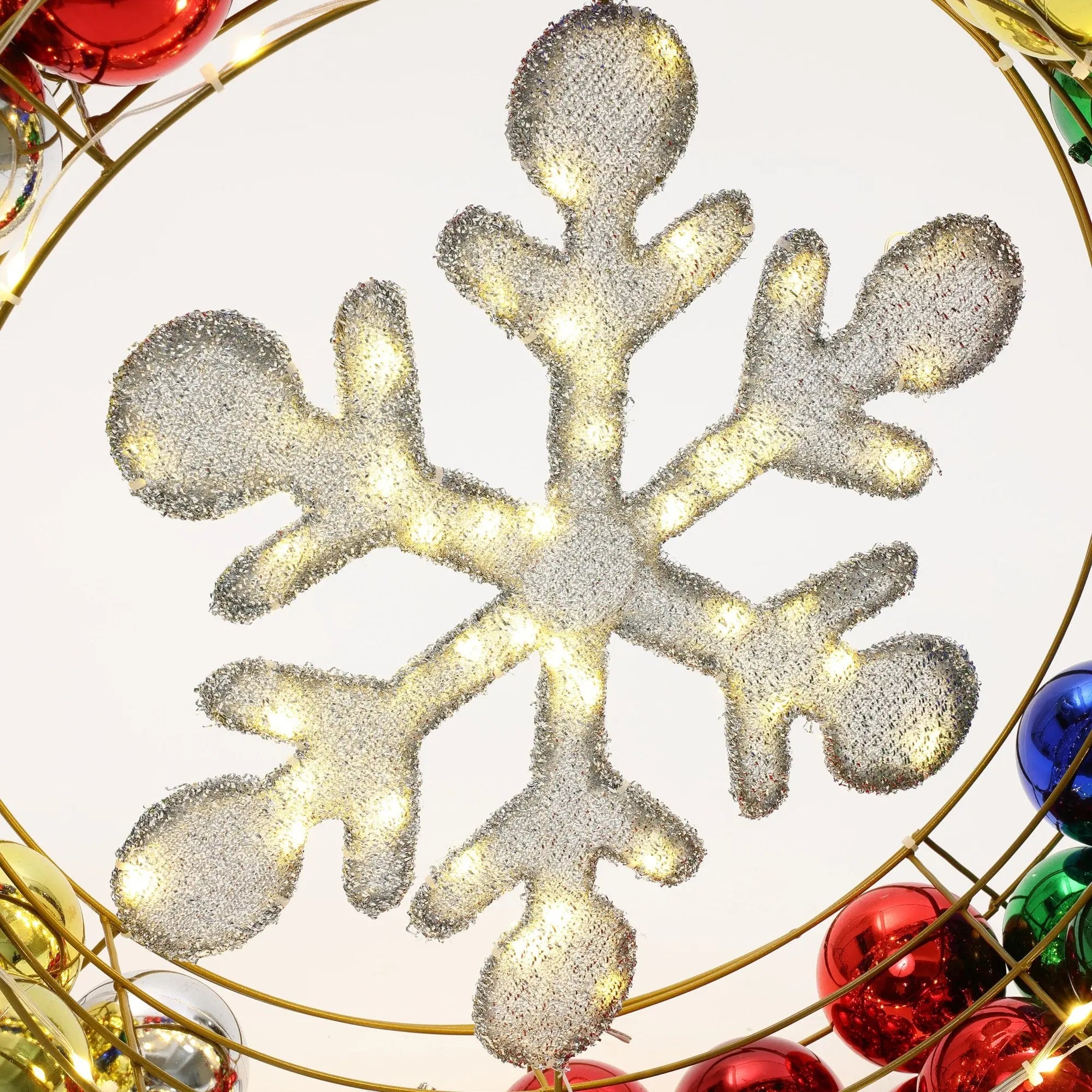 A large illuminated snowflake decoration surrounded by red, green, and blue baubles serves as the perfect holiday decoration, reminiscent of a festive Christmas wreath.