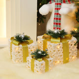 3 silver tinsel gift boxes with bows, pine accents are arranged under Christmas tree on white furry rug.