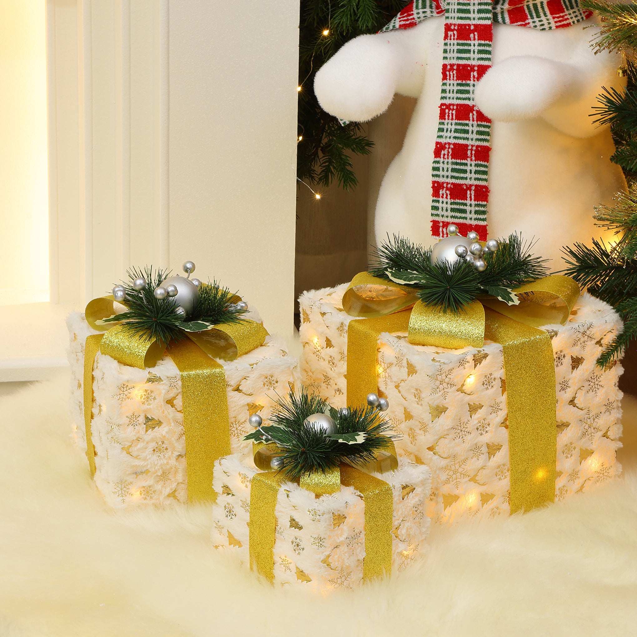 3 silver tinsel gift boxes with bows, pine accents are arranged under Christmas tree on white furry rug.