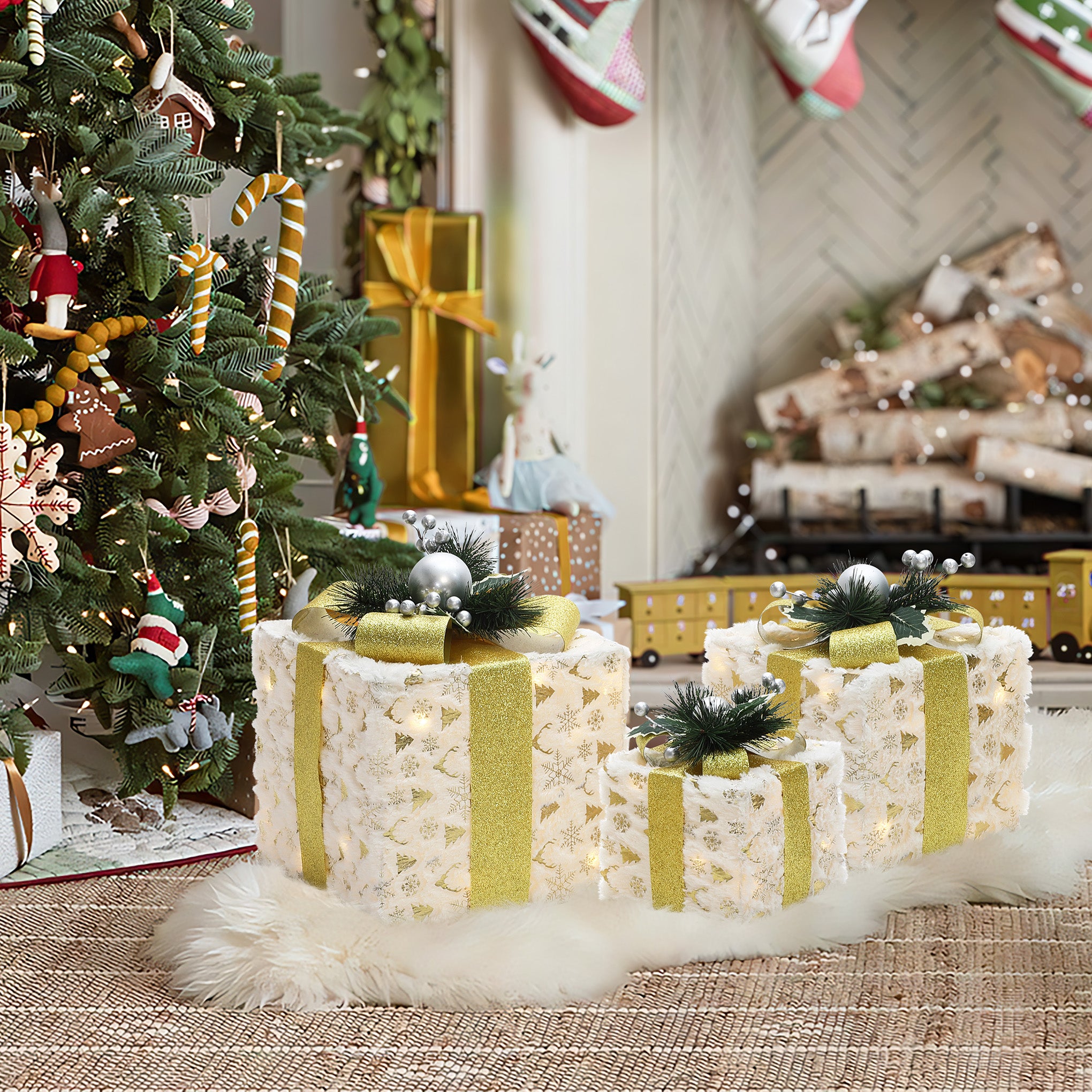 3 pre-lit holiday silver tinsel gift boxes with gold ribbons,white rug near christmas tree , fireplace adorned with stockings.