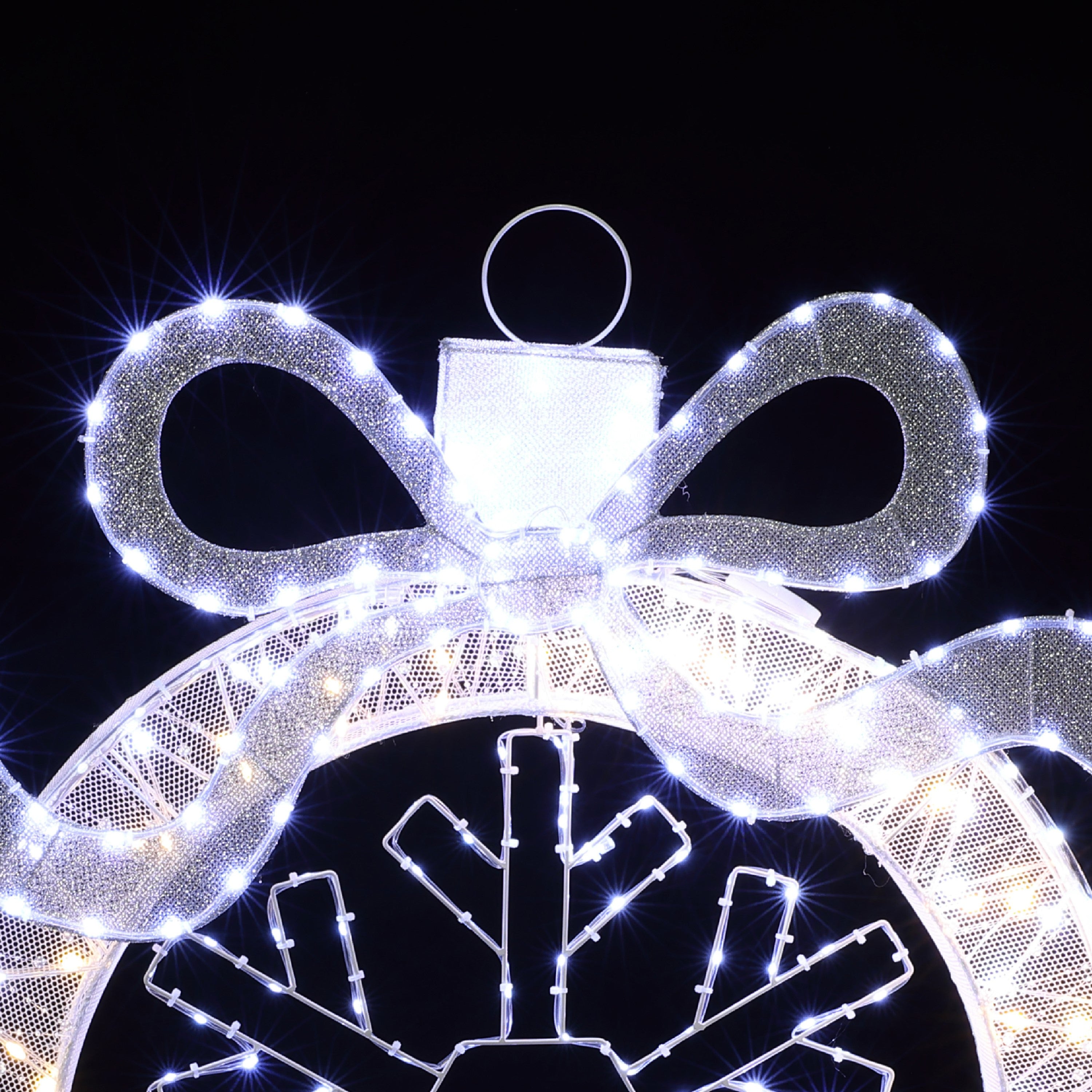 Close-up of decor holiday ornament with large silver bow, illuminated by white lights.