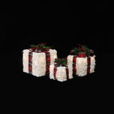 3 white, textured gift boxes with red plaid ribbons, displayed with holiday decor against black background.