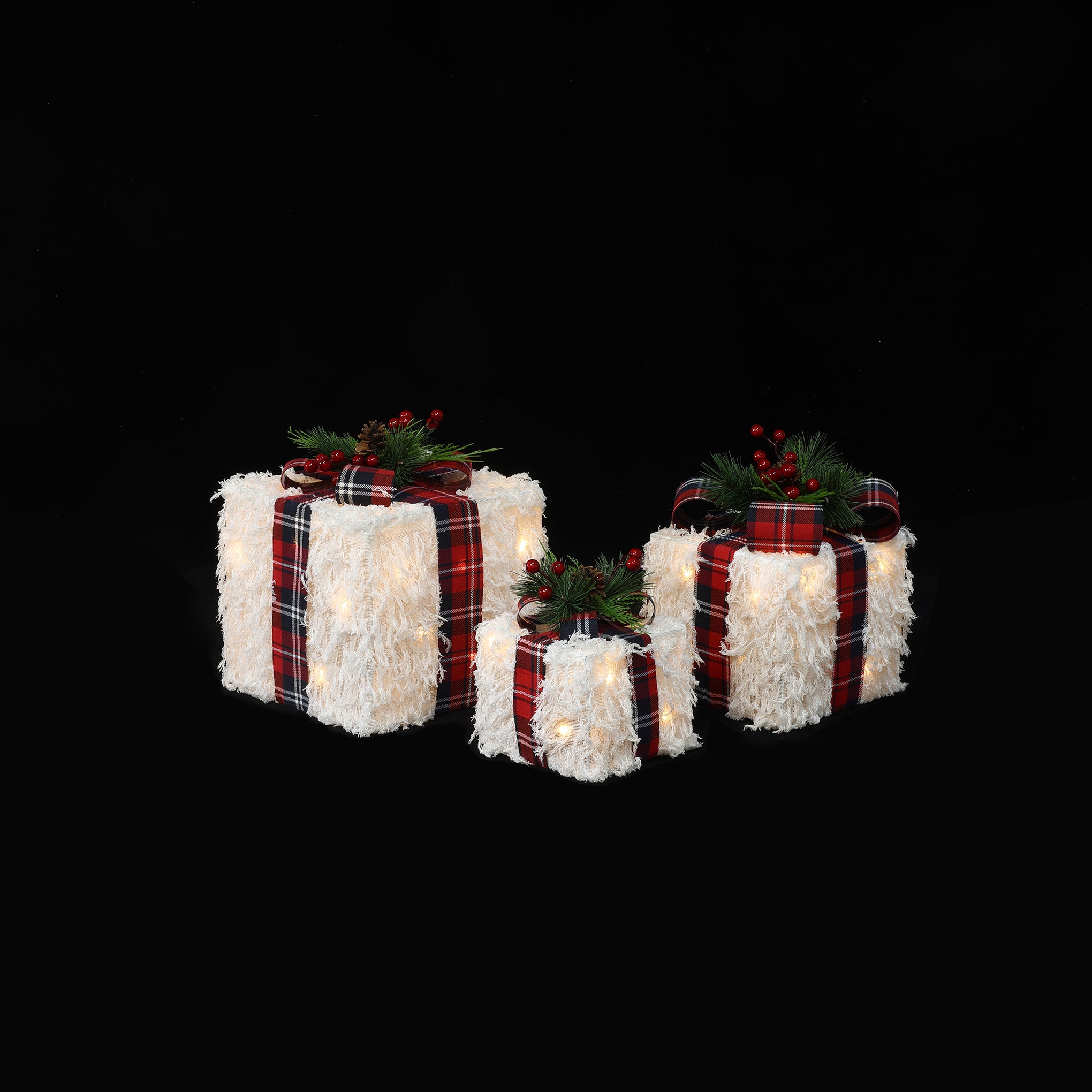 3 white, textured gift boxes with red plaid ribbons, displayed with holiday decor against black background.