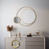 Decorative wall with circular mirrors featuring golden frames above a beige dresser. Pampas grass in a vase, abstract sculptures, and a round lamp imbue the space with modern elegance.