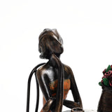 Bronze sculpture of a seated woman with head tilted back, wearing a strapless dress, captures romantic moments next to a vase of flowers.