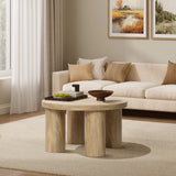 A cozy living room with a beige sofa, oak-finish coffee table, decorative bowl, books, and a green vase. Two landscape paintings hang on the wall above the sofa.