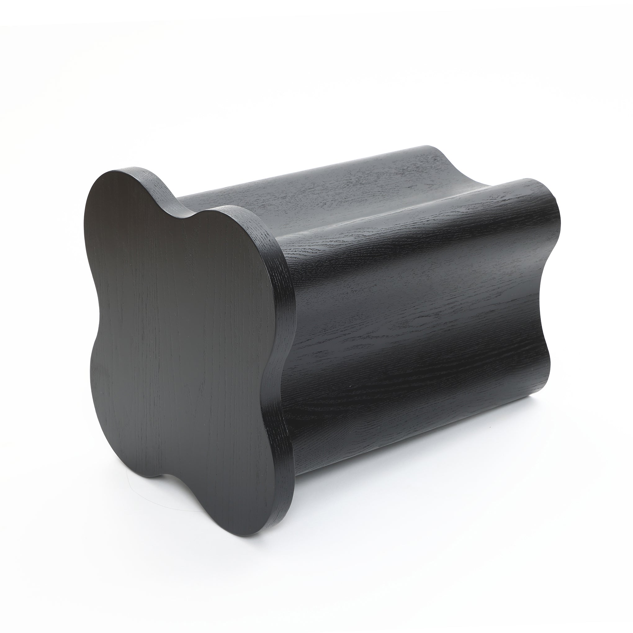 A black cloverleaf shape, wavy-edged stool crafted from premium MDF wood with a glossy finish, positioned on its side against a white background.