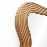 Curved rattan mirror frame with a modern vibe against a white wall.