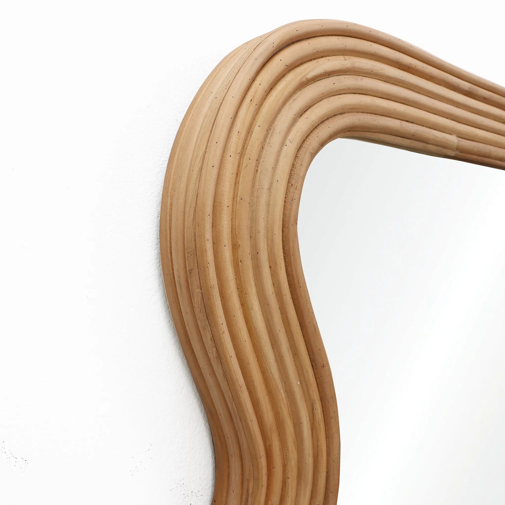 Curved rattan mirror frame with a modern vibe against a white wall.