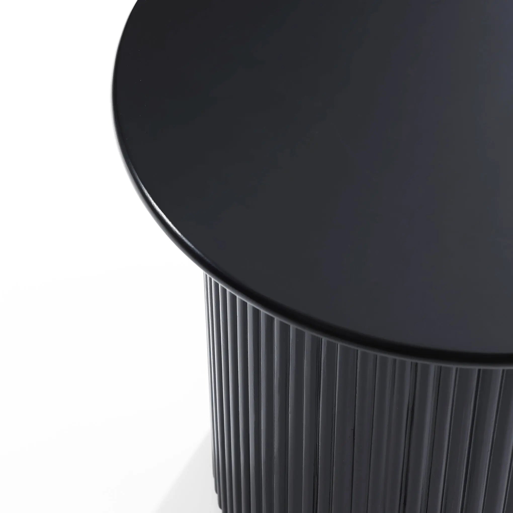 Close-up of a sleek, black round side table with a ridged cylindrical base and smooth tabletop, showcasing its decorative effect that complements any modern style.