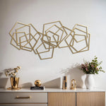 Gold iron metal wall art with abstract shapes hangs elegantly above a white and wood sideboard adorned with decorative items, including flowers and a book.