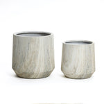 A stylish planter set features two ribbed, cylindrical stone planters of differing sizes, placed side by side against a white background. Each boasts a unique marble ribbed texture and comes with a drainage hole for optimal plant care.