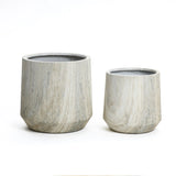 A stylish planter set features two ribbed, cylindrical stone planters of differing sizes, placed side by side against a white background. Each boasts a unique marble ribbed texture and comes with a drainage hole for optimal plant care.