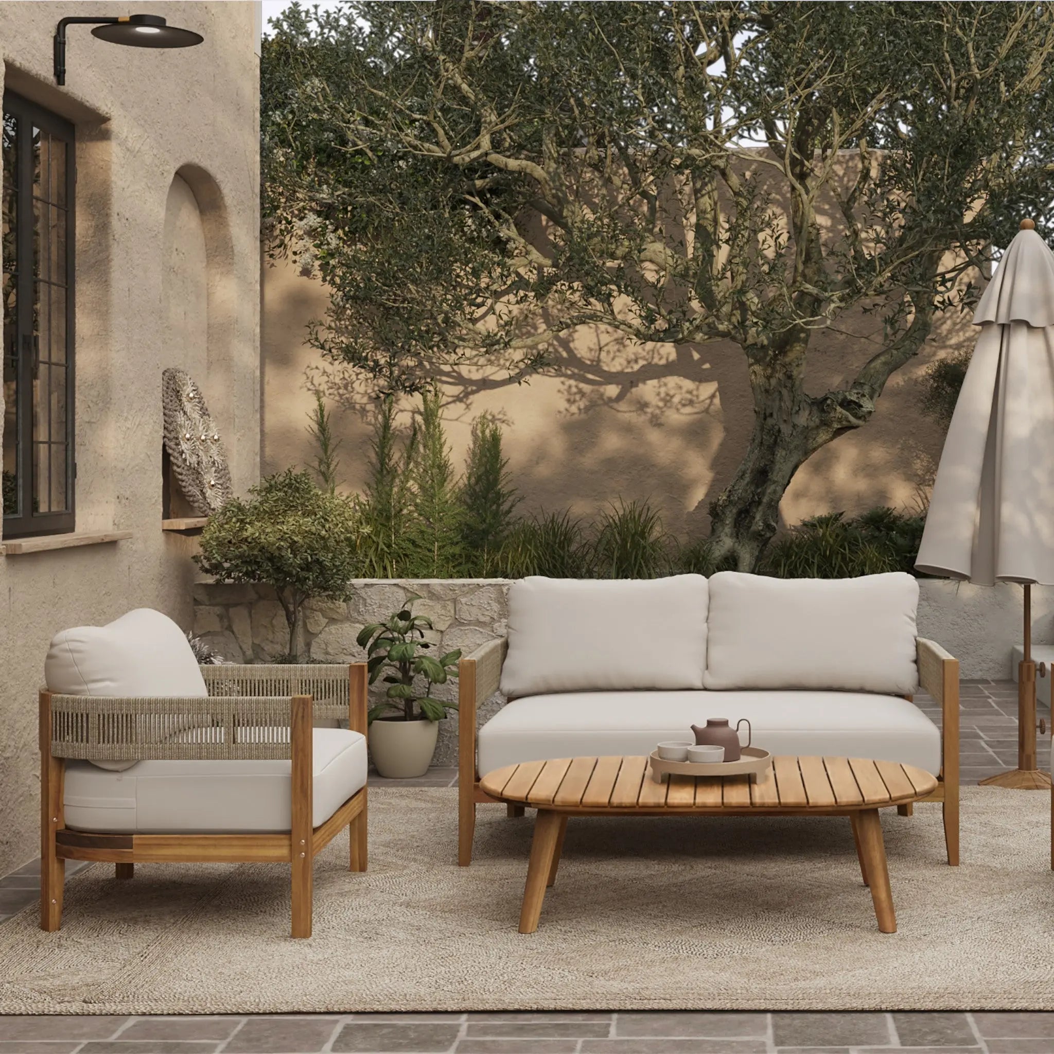 Outdoor patio with beige cushioned chairs, a Rope Sides Loveseat, wooden coffee table with teapot and cups, potted plants, and an umbrella on a woven rug—Club-Style Patio Furniture set against stucco walls and trees.