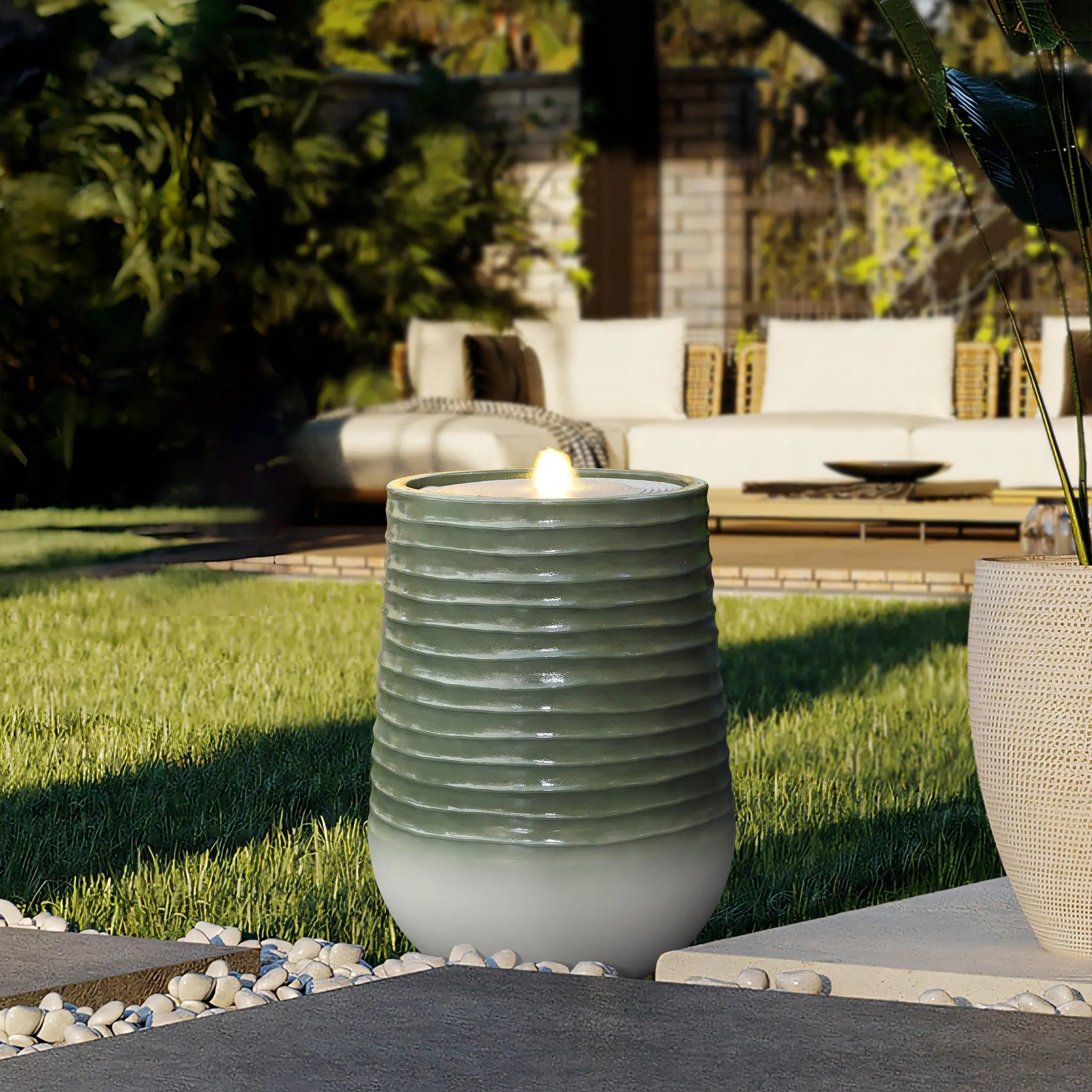 A lit outdoor gas lamp with a ribbed design stands on a patio with a grassy area and wicker seating in the background, subtly illuminated by LED lights.
