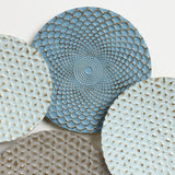 Four decorative plates with textured patterns and shades of blue and gray are displayed overlapping each other, creating an abstract wall art piece that adds depth to any room.