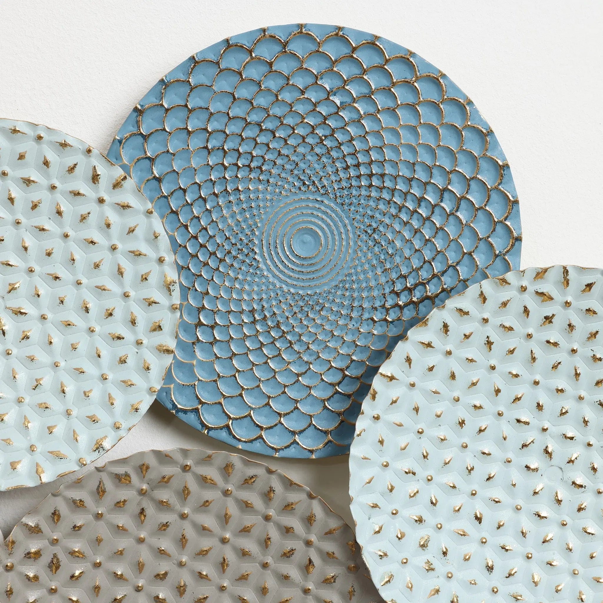 Four decorative plates with textured patterns and shades of blue and gray are displayed overlapping each other, creating an abstract wall art piece that adds depth to any room.