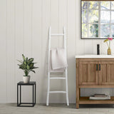 A bathroom exuding rustic charm features a fir wood vanity, a white blanket ladder with a towel, a potted plant on a small table, and a window framing the serene view of the tree outside.