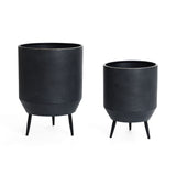 Two cachepots with a distressed black finish are displayed, featuring textured surfaces and standing on three-legged metal bases against a white background.