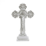 A decorative white crucifix, embodying the Christian faith, features an intricate design with a central figure of Jesus, elegantly standing on a rectangular base—perfect for religious occasions.