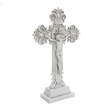 White ornate cross featuring a depiction of Jesus crucified, ideal for religious occasions. Detailed designs grace the ends, with inscriptions visible above Jesus. This symbol of Christian faith stands proudly on a rectangular base.