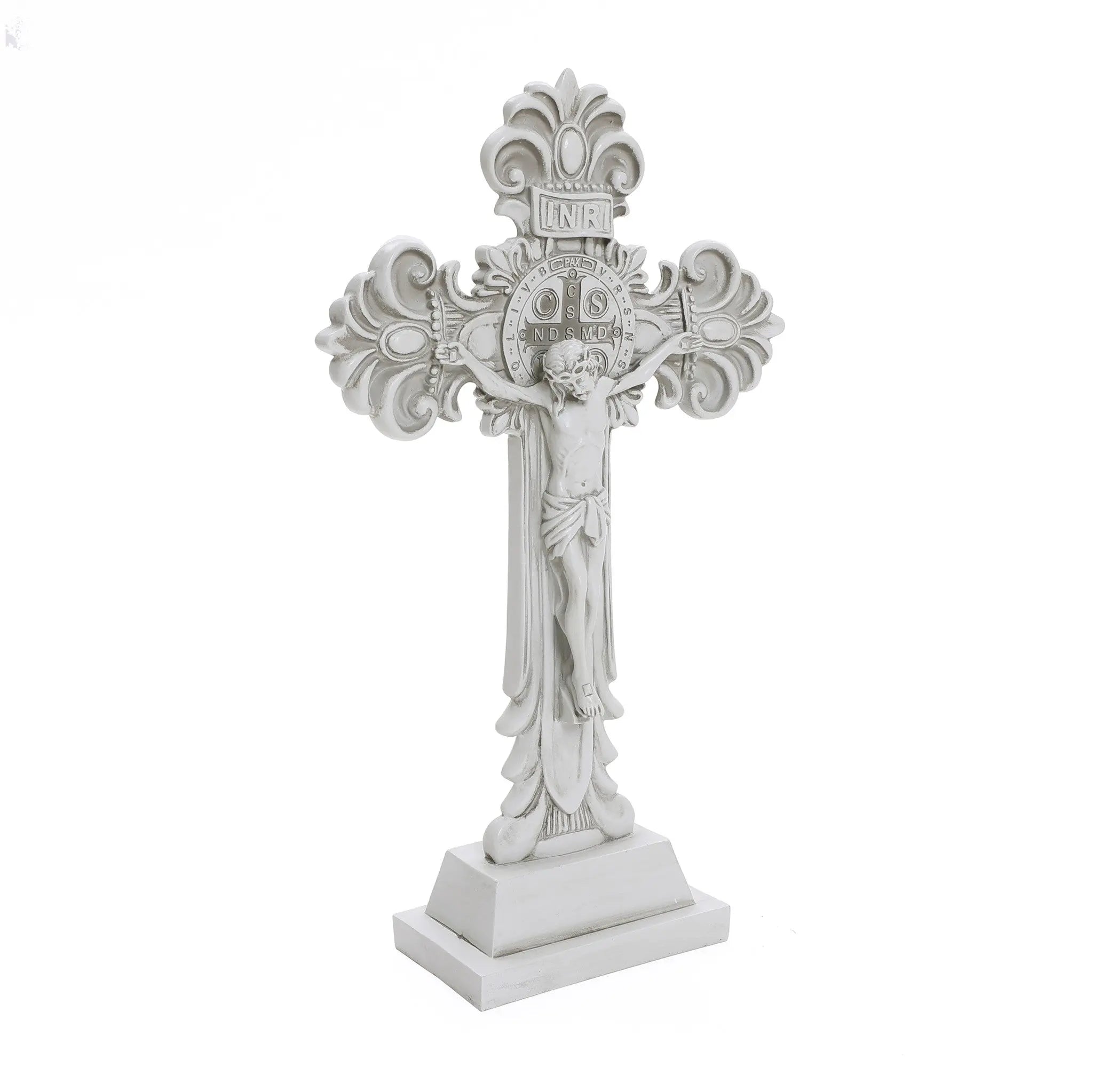 White ornate cross featuring a depiction of Jesus crucified, ideal for religious occasions. Detailed designs grace the ends, with inscriptions visible above Jesus. This symbol of Christian faith stands proudly on a rectangular base.