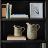 Books and a framed photo grace the shelf, flanked by two ceramic pitchers with a terracotta finish, showcasing artisanal craftsmanship.