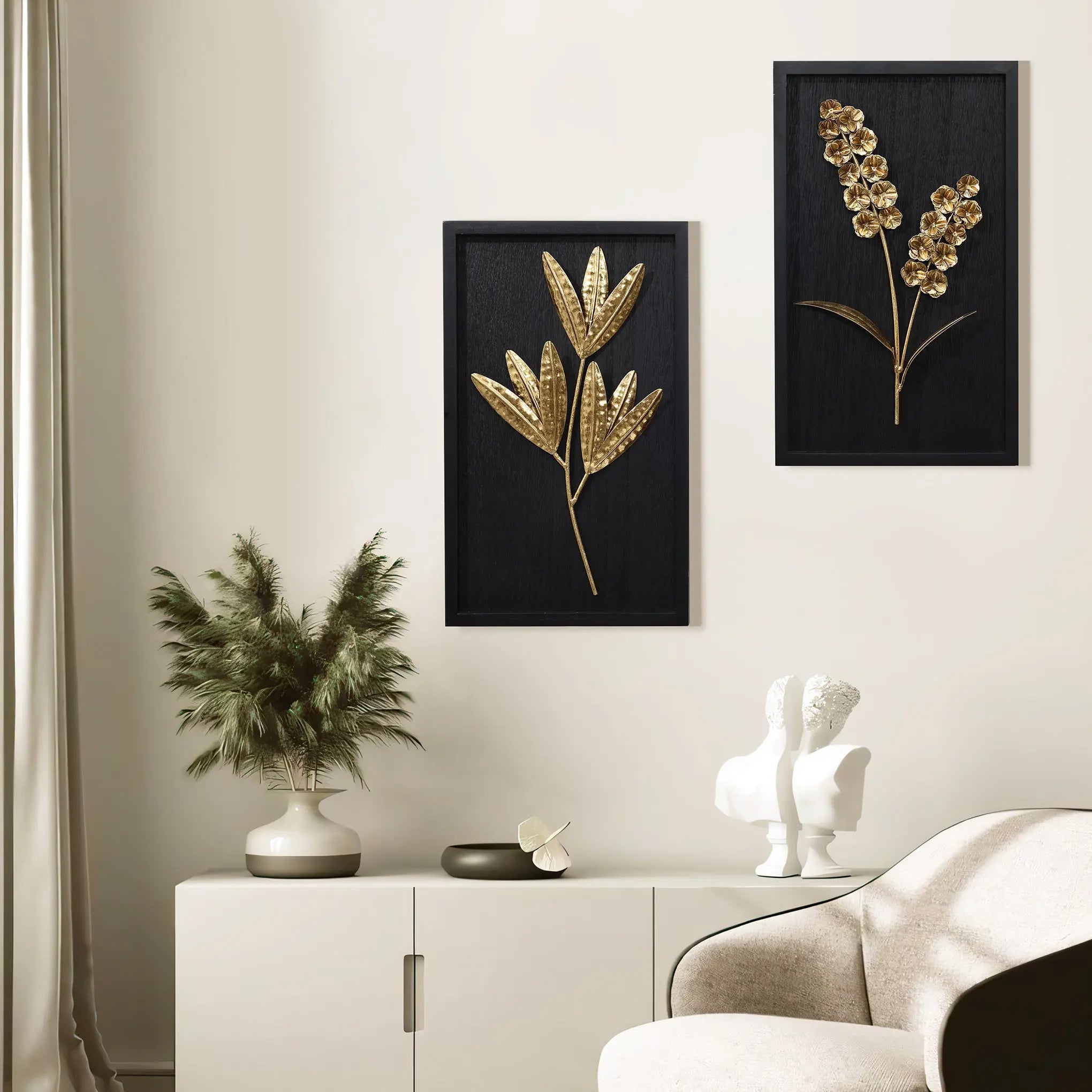 Minimalist interior design featuring a white chair, a sideboard, two gold-on-black botanical wall art pieces, a vase with greenery, and a sculptural decoration.