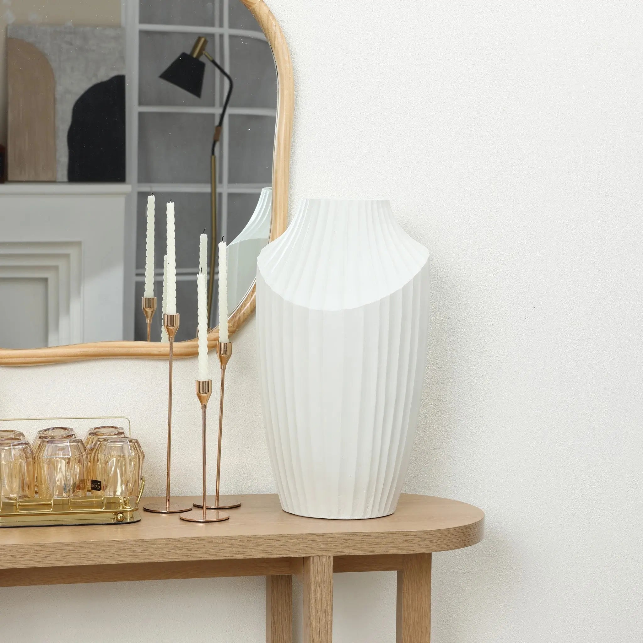 The contemporary home decor features a white fluted vase as a decorative piece on a wooden table, accompanied by a gold candle holder with thin candles, and a tray with glasses. A mirror reflects the lamp and room details.