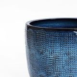 A close-up showcases the LuxenHome Ocean blue glazed round ceramic planter, 13.98 h, featuring a textured surface with a rich, glossy blue finish. Its intricately designed top edge stands out against a plain white background, enhanced by a subtle gradient for an elegant look.