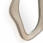 This modern home decor piece features an oval, irregularly shaped wall mirror with a natural finish wood frame, offering a glimpse of sophistication when mounted on the wall.
