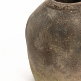 A close-up view of an aged, weathered ceramic pot with a handcrafted finish and muted color on a white background, embodying the rustic charm of a vintage terracotta vase.
