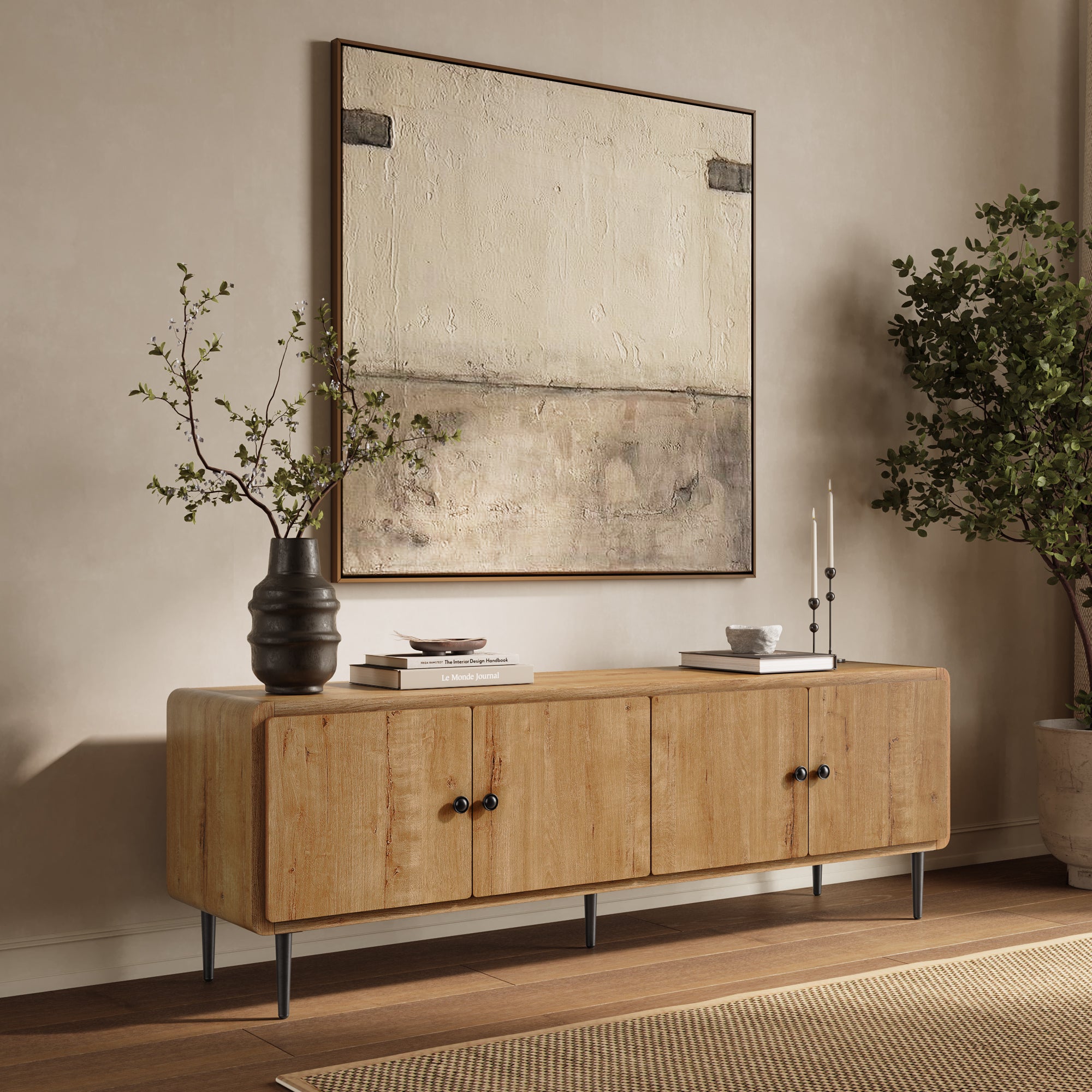 Minimalist TV stand with black legs stands against a beige wall, topped with books, candles, and a vase with branches.
