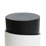 A cylindrical black object with a textured surface is partially inserted into a white sleeve featuring a unique white irregular pattern, set against a plain background.