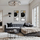 A modern living room features a gray sectional sofa, a luxurious fur throw, and a round coffee table adorned with books. The space boasts modern abstract wall decor in black, white, and gold hues, complemented by a chic chandelier and large windows that flood the room with natural light.