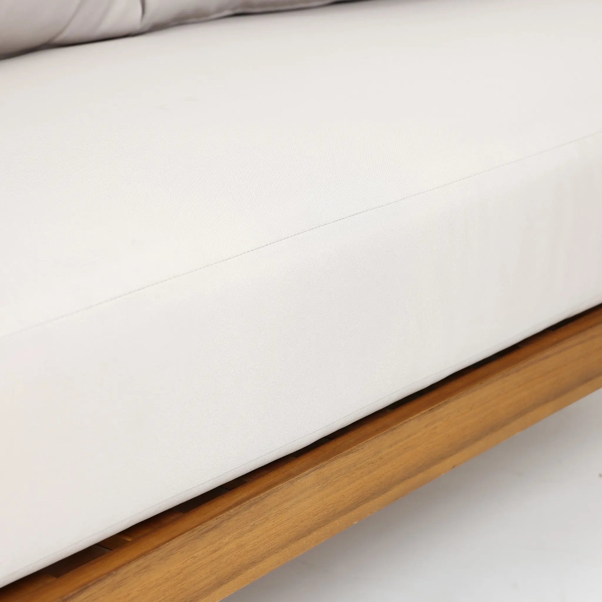 Close-up of a white cushion on an Outdoor Acacia Wood sofa frame, with a portion of a gray pillow visible at the top—perfectly paired with a Rope Sides Loveseat or Coffee Table Set for your patio.