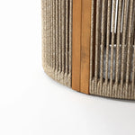 Close-up of a drum-shaped round end table featuring hand-woven rope and vertical slats, supported by a natural acacia wood beam on a white background.