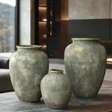 Displayed on a table in a modern interior setting, three large textured ceramic vases vary by size and feature an antique look. The charming scene includes a window and contemporary decor elements, highlighted by LuxenHomes rustic gold and brown terracotta bud vase, 8.7 h.