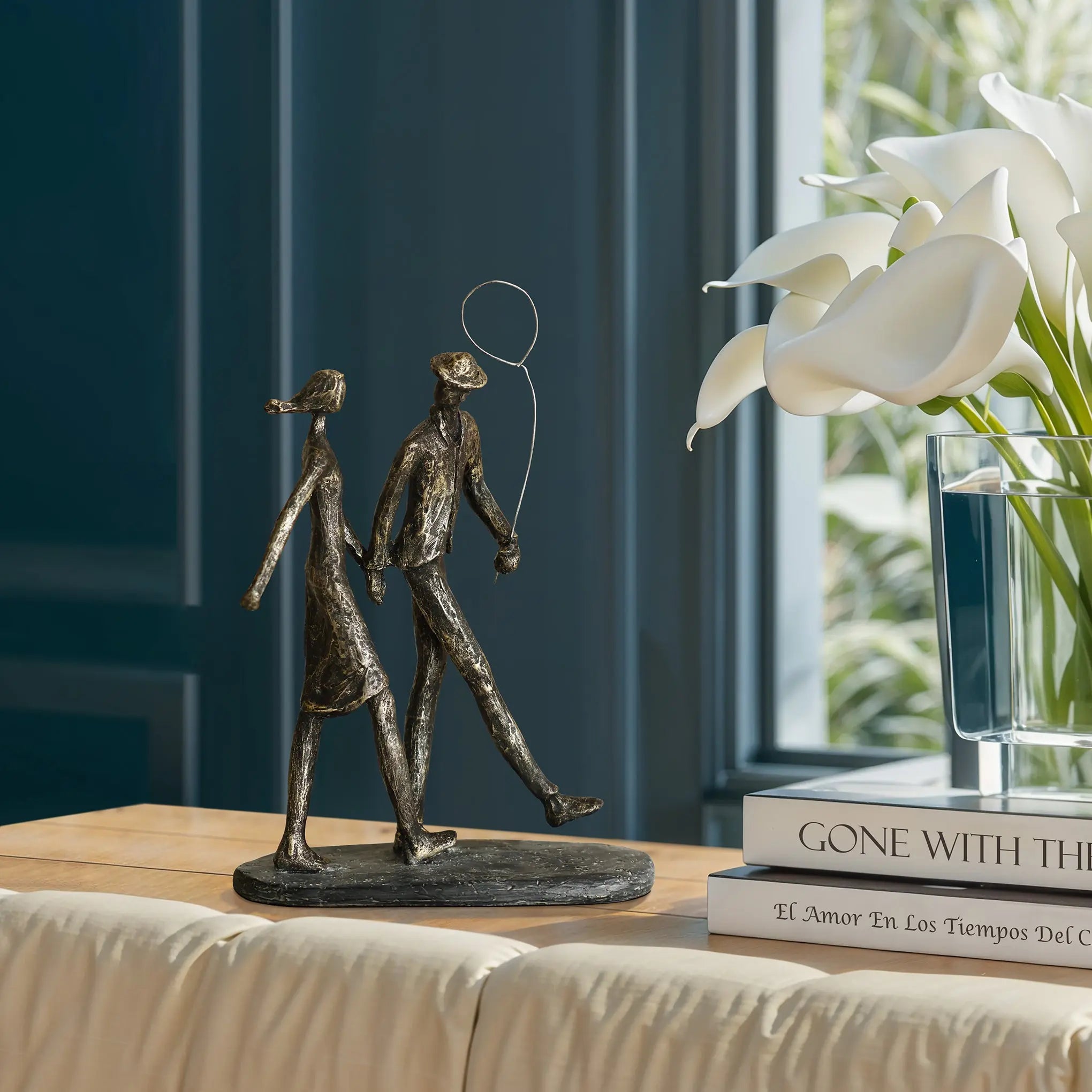 A modern resin sculpture of a couple walking with a balloon complements the stack of books and white calla lilies on the table.