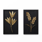 Two black framed artworks with gold botanical reliefs enhance your interior design: one features elongated leaves, while the other showcases clustered flower bouquets.