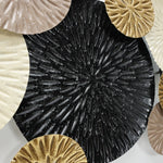 Close-up of overlapping decorative plates with radial patterns in black, gold, beige, and cream colors, reminiscent of nature-inspired artwork.