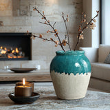 A green and white stoneware vase with decorative branches sits on a table beside a lit candle, adding to the rustic design of the cozy living room.