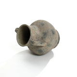 An aged earthenware jug lies on its side against a plain white background, resembling a LuxenHome Rustic mottled grey terracotta urn vase with handles, 12.1 h, featuring a rounded body, two small handles, and a narrow neck with a weathered appearance.