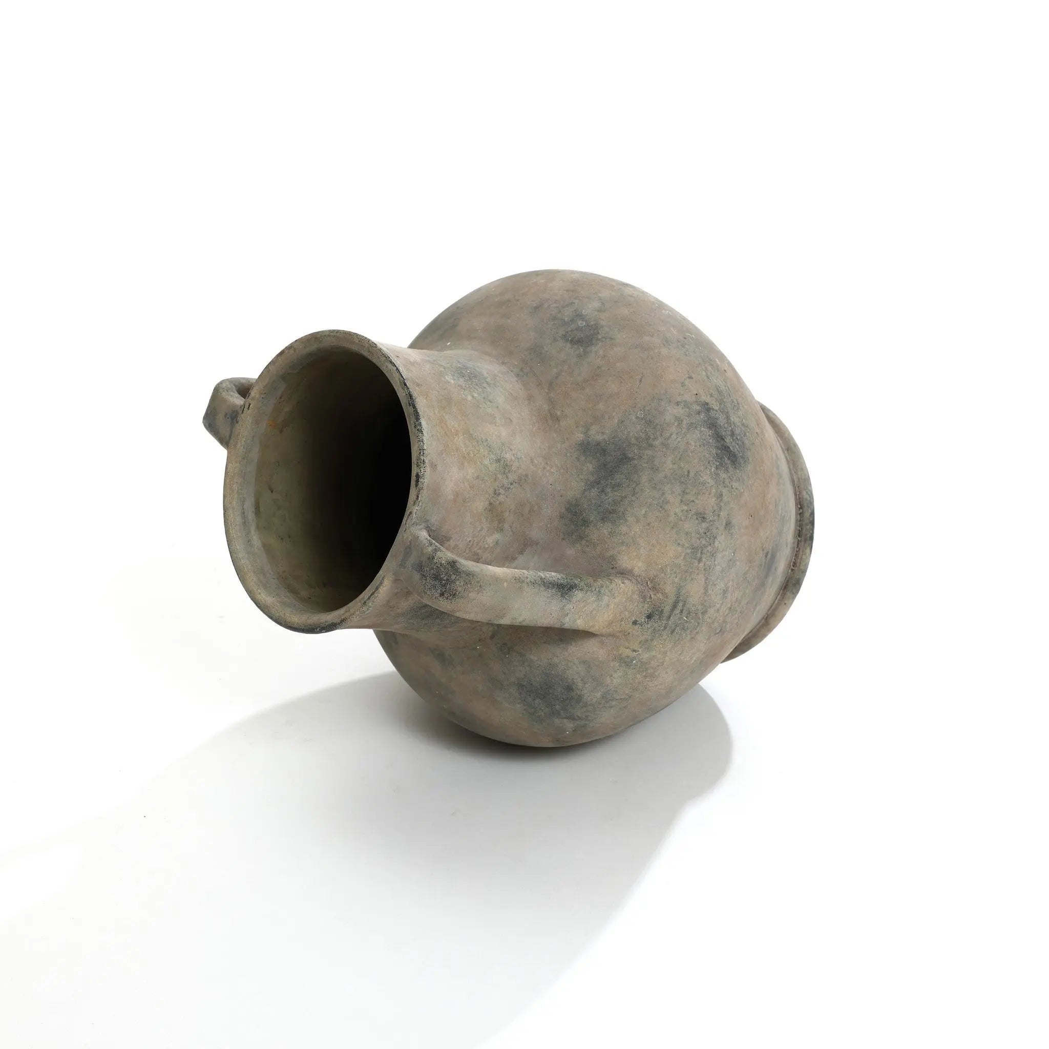 An aged earthenware jug lies on its side against a plain white background, resembling a LuxenHome Rustic mottled grey terracotta urn vase with handles, 12.1 h, featuring a rounded body, two small handles, and a narrow neck with a weathered appearance.