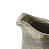 A close-up of a rustic, handmade clay pitcher vase showcases its textured, uneven rim and dark, earthy glaze, reflecting artisanal craftsmanship.