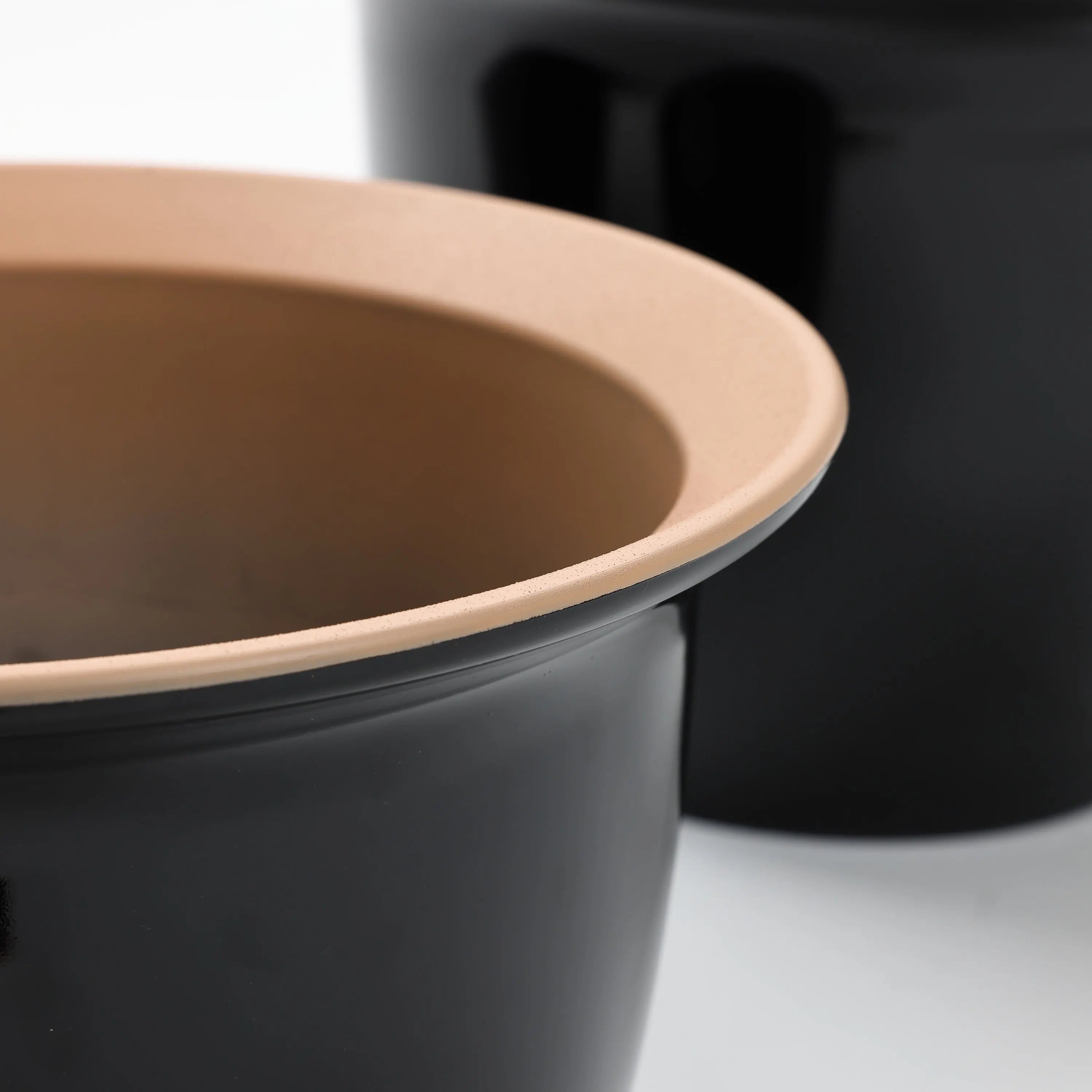 Close-up of a black planter pot with a beige rim, artfully overlapping another in the background, part of a decorative set perfect for indoor and outdoor use.