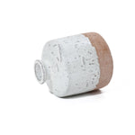 A ceramic jug, with a bottle-like design, lies on its side, showcasing a textured surface and a blend of white glaze with a natural clay base.