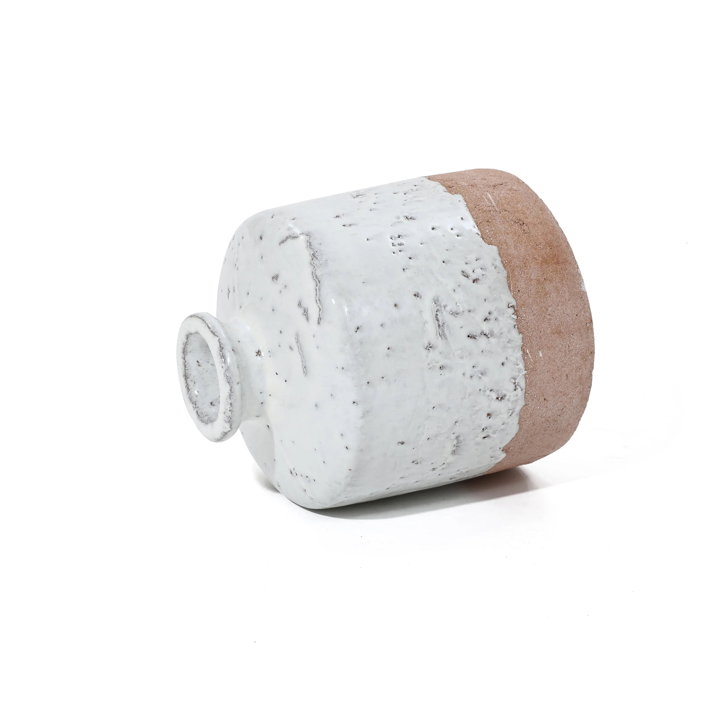 A ceramic jug, with a bottle-like design, lies on its side, showcasing a textured surface and a blend of white glaze with a natural clay base.